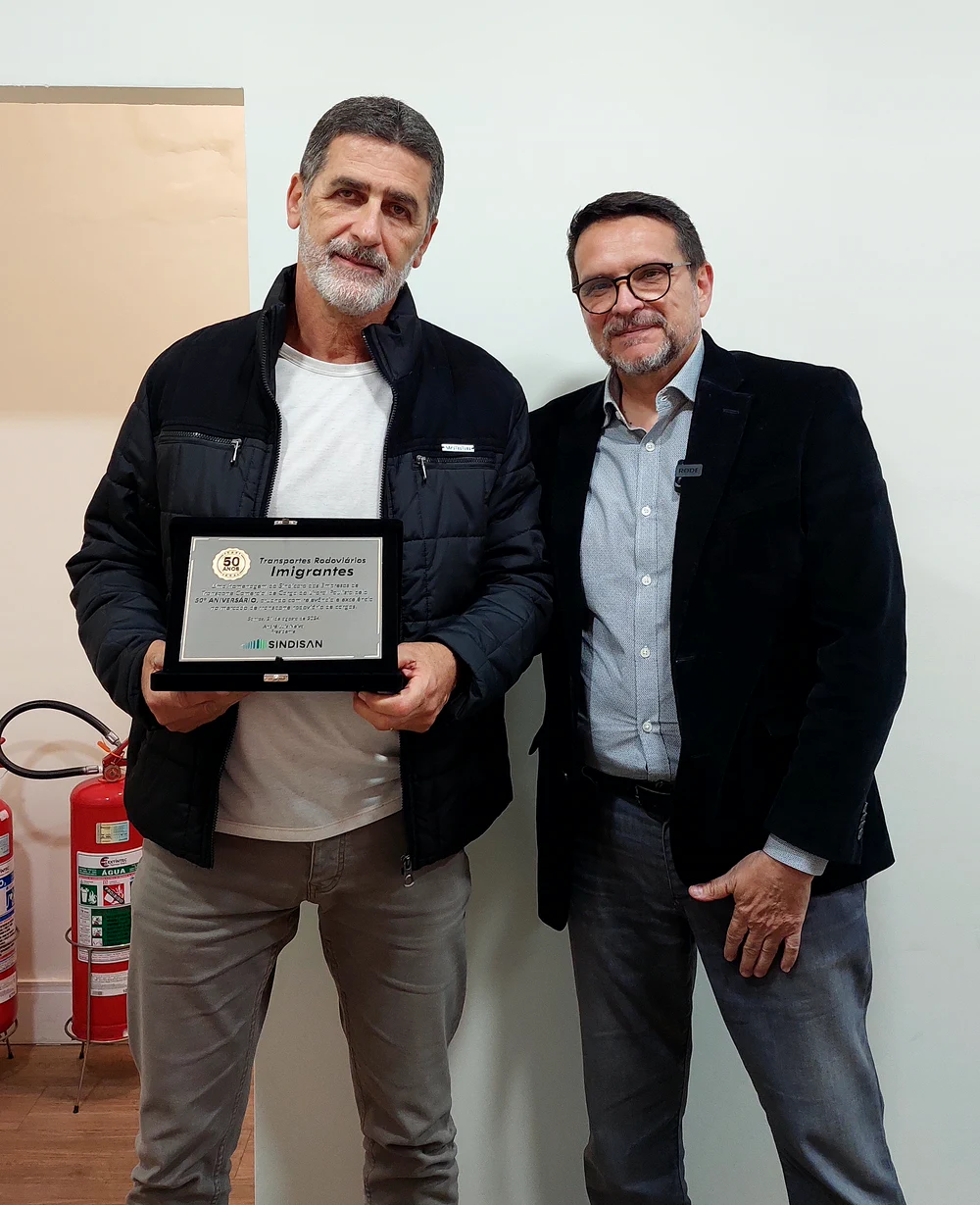 Marco, à frente da Transportes Rodoviários Imigrantes, ao lado do presidente do SINDISAN, segurando a placa comemorativa dos 50 anos