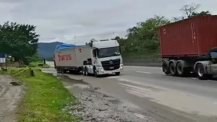 Caminhões da frota transportando contêineres em rodovia, com a serra do mar ao fundo