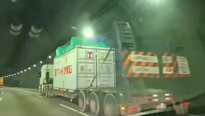 Comboio de caminhões com contêineres atravessando um túnel iluminado na serra